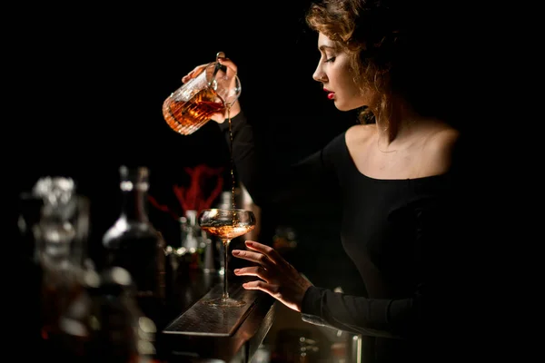 Привлекательная бармен в темном баре мягко наливает коктейль в бокал . — стоковое фото