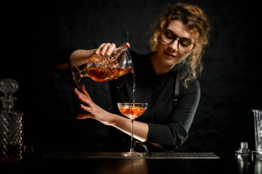 Genç bayan barmen kadehi bardağa karıştırarak profesyonel olarak kokteyl dolduruyor..