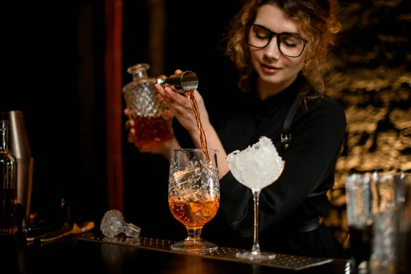 Young female barman accurate pours drink from jigger into mixing cup. — Stock Photo, Image