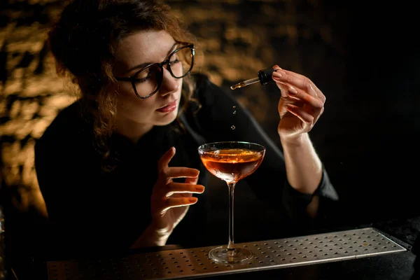 Beautiful woman at bar attentively adds ingredient to glass with drink — Stock Photo, Image