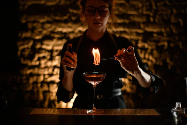 Garota barman detém pinças com queima de plantas sobre vidro . — Fotografia de Stock