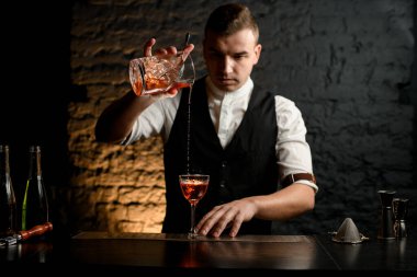 Bardaki genç barmen dikkatle bardağa kokteyl dolduruyor.