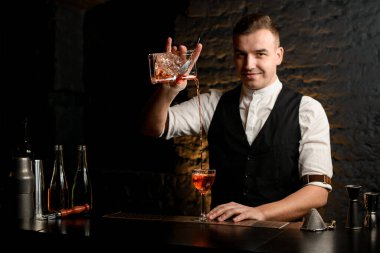Bardaki gülümseyen genç barmen bardağa kokteyl doldurur.