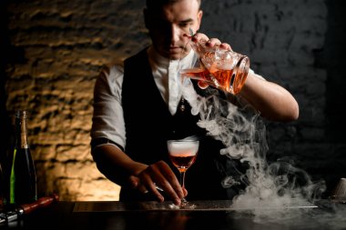Yakın plan. Bardaki adam profesyonel olarak dumanlı bardağa kokteyl dolduruyor.