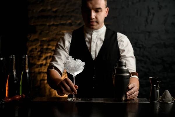 Barman sostiene vidrio transparente lleno de hielo que se encuentra en el mostrador de la barra . — Foto de Stock