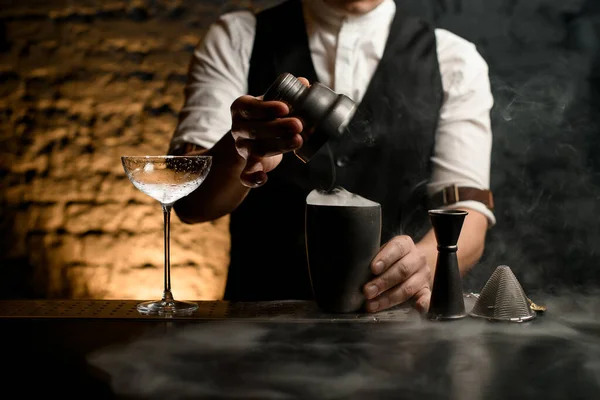 Närbild man bartender håller i sin hand locket från stål shaker med rök på rökig bar. — Stockfoto