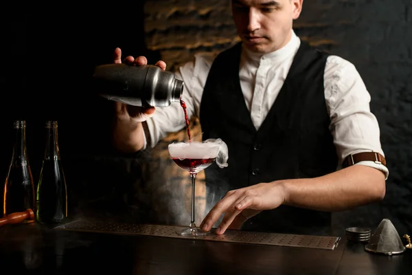 Professionele man barman voorzichtig gieten cocktail van roestvrij shaker in rokerig glas — Stockfoto