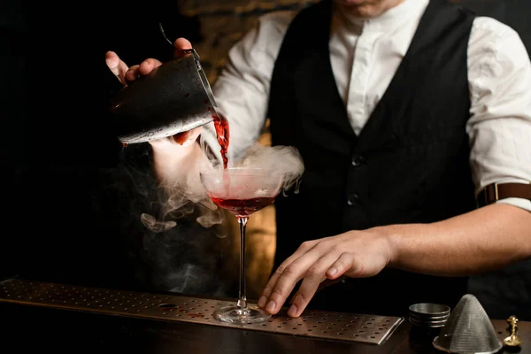 Primer plano. Hombre en el bar verter suavemente cóctel de agitador de acero inoxidable en vidrio ahumado — Foto de Stock