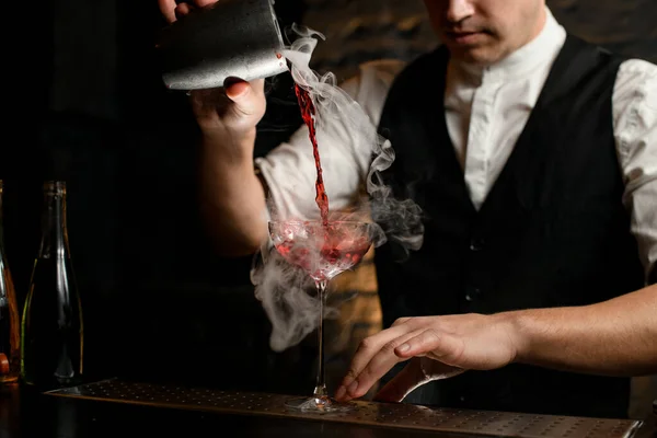 Close-up. Man at bar gently pouring drink from stainless shaker into smoky glass — Stock Photo, Image