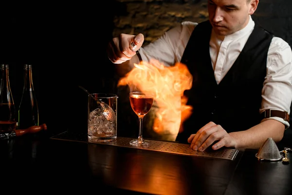 Primo piano. L'uomo a bar spruzza esatti su vetro con cocktail e fa il fuoco . — Foto Stock