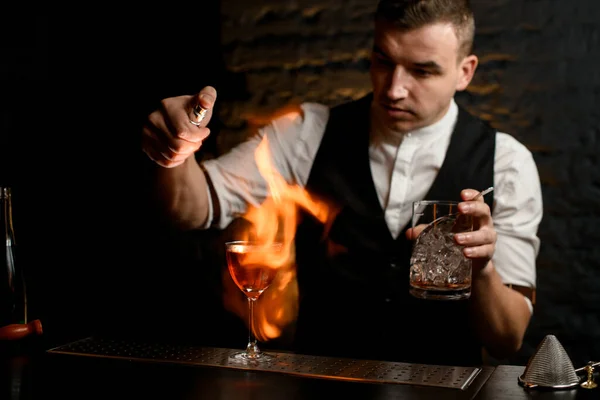 Primo piano. L'uomo al bar spruzza delicatamente su vetro con cocktail e accende il fuoco . — Foto Stock