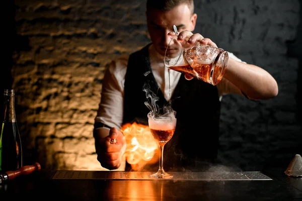 Close-up. Barman profissionalmente derrama coquetel para polvilhar vidro fumegante para ele e fazer fogo . — Fotografia de Stock
