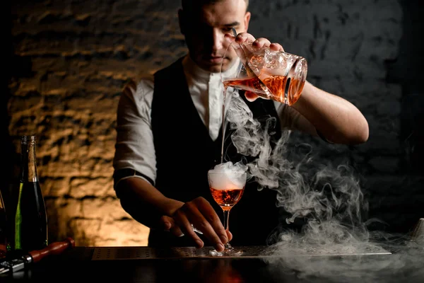 Close-up. Barman professionally pours cocktail to smoky glass — Stock Photo, Image