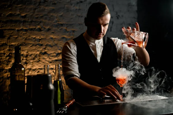 Zbliżenie. Profesjonalny barman nalewa koktajl do dymiącego szkła — Zdjęcie stockowe