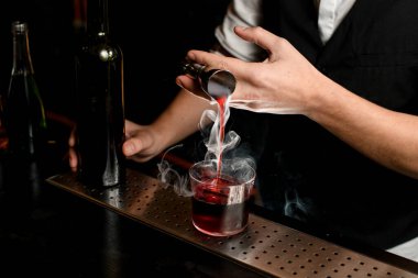 Yakın plan. Barmenler ustaca doldurur dumanlı içeceği jiggerdan buzlu cama