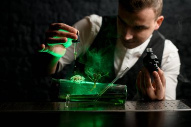 Barmen nazikçe içinde yeşil sıvı olan cam şişeye malzeme ekliyor ve şuna bak..