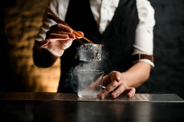 Nahaufnahme. Barkeeper hält Pinzette mit Eis über dampfendem Glas in der Hand — Stockfoto