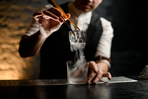 Close-up. Homem barman suavemente segura na mão pinças com gelo sobre vidro fumegante — Fotografia de Stock