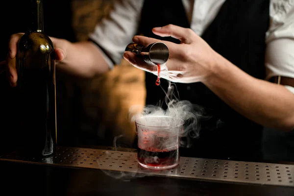 Крупным планом. Бармены аккуратно наливают курящий напиток из стакана в стакан со льдом — стоковое фото