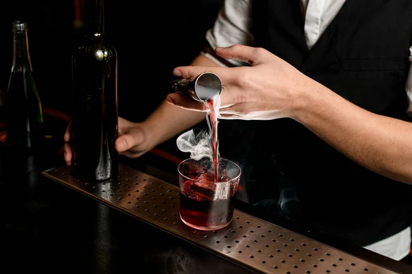 Közelkép. A csapos óvatosan önti a füstös italt a jiggerből az üvegbe jéggel. — Stock Fotó