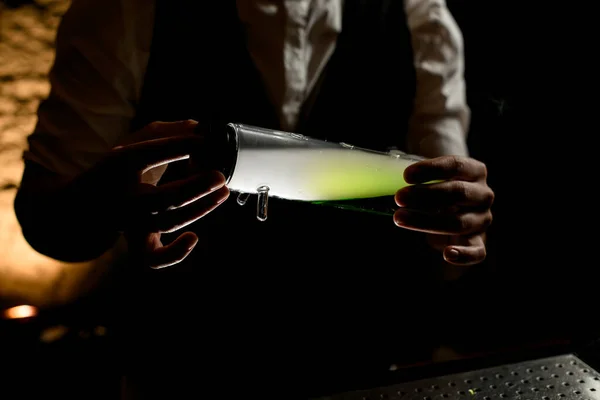 Κοντινό πλάνο. Man bartender κρατά στα χέρια του φωτιζόμενη γυάλινη φιάλη σχεδιαστή με καπνιστό πράσινο υγρό μέσα — Φωτογραφία Αρχείου