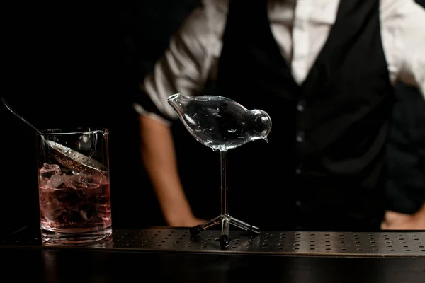 Beauty glass vessel in shape of bird and cup with cocktail stands on bar counter