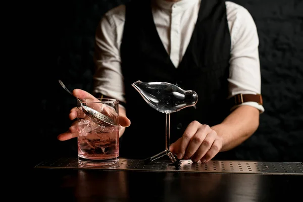 Close-up mannelijke barman met glazen mengbeker en glazen vat in de vorm van een vogel staat in de buurt — Stockfoto