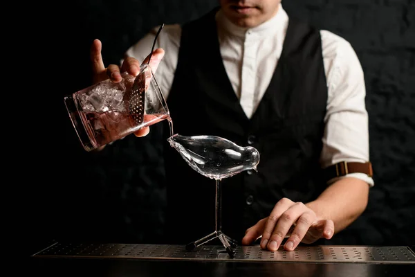 Barman z bliska nalewający napój ze szklanego kubka do szklanego naczynia w kształcie ptaka — Zdjęcie stockowe