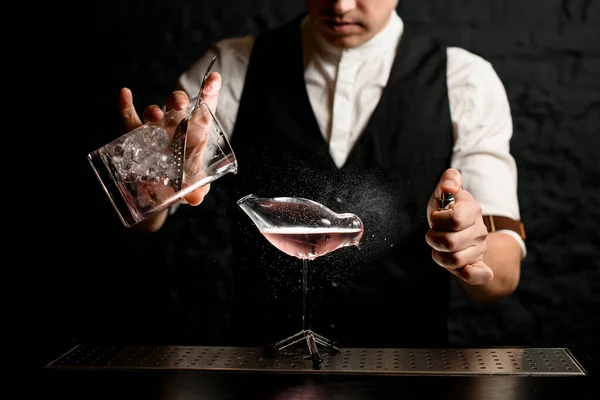 Крупным планом бармен наливает напиток из стеклянной чашки в стеклянный сосуд в виде птицы и брызгает на него — стоковое фото