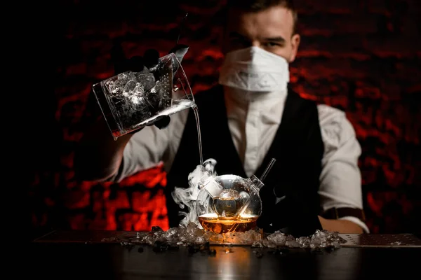 Joven barman en máscara con guantes negros vierte bebida en frasco de diseñador especial — Foto de Stock