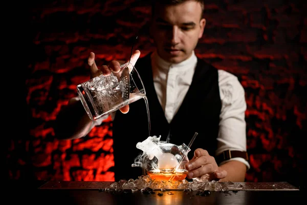 Uomo barman versa professionalmente bevanda fredda in boccetta fumosa designer — Foto Stock