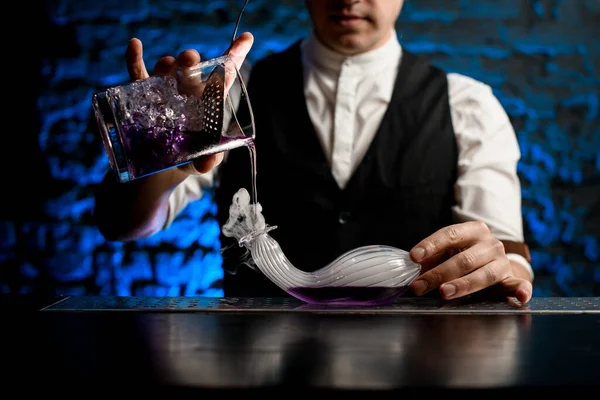 Крупным планом бармен наливает напиток из стеклянной чашки в дымчатую стеклянную фляжку необычной формы — стоковое фото