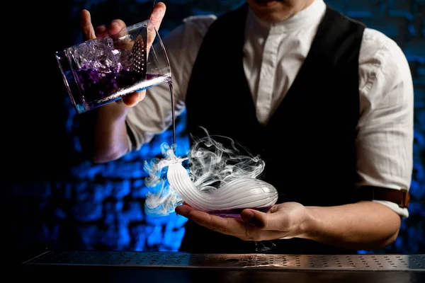 Κοντινό πλάνο μπάρμαν αριστοτεχνικά ρίχνει ποτό από το ποτήρι ανάμειξη σε καπνιστή γυάλινη φιάλη ασυνήθιστο σχήμα στο χέρι του — Φωτογραφία Αρχείου