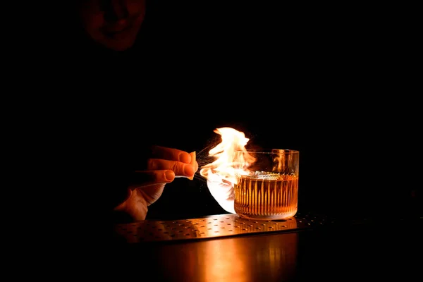 Close-up bartender sprinkles citrus juice on glass with cocktail and sets it on fire. — Stock Photo, Image