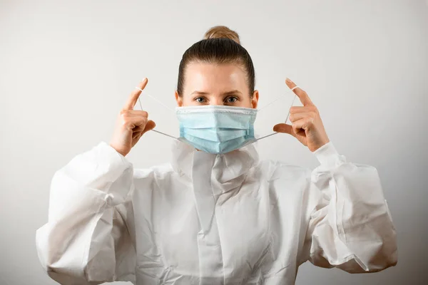 Молодая женщина в белом защитном костюме аккуратно надевает медицинскую маску — стоковое фото