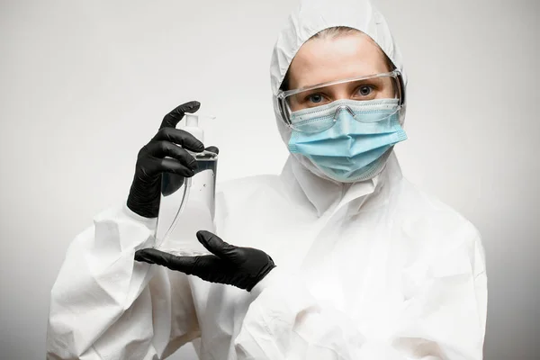 Jeune femme en vêtements de protection médicale complète avec des gants en latex noir tient désinfecteur dans ses mains . — Photo
