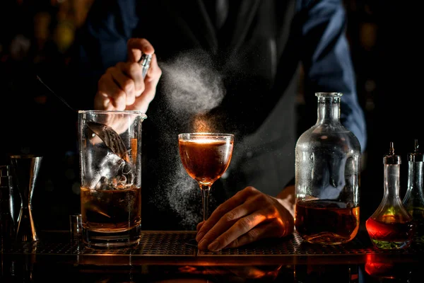 Barman drží sklenici nápoje s rukou a sype na ni — Stock fotografie