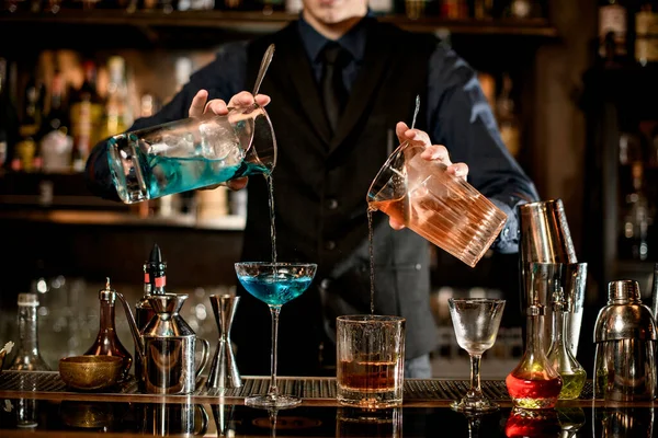 Junger Barkeeper gießt professionell Cocktails in Gläser. — Stockfoto