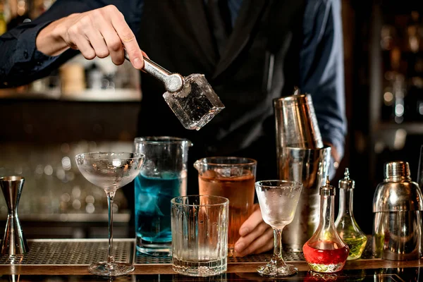Bartenders mão segura pinças com grande pedaço quadrado de gelo — Fotografia de Stock