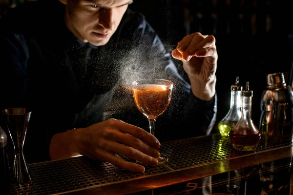 Молодой бармен побрызгает алкогольным коктейлем кусочком цитрусовой цедры — стоковое фото