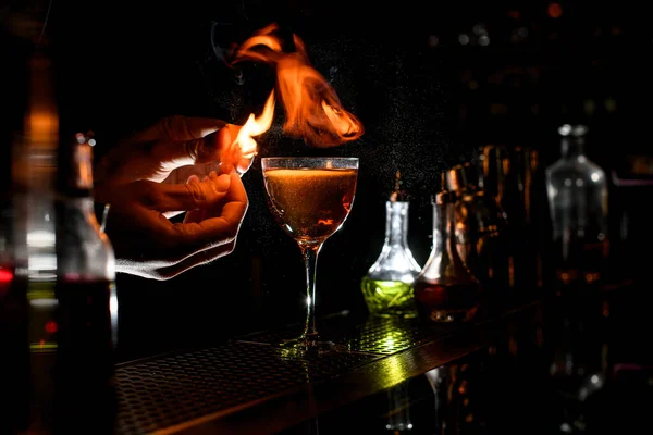 Close-up bartender polvilhe para coquetel alcoólico com pedaço de raspas cítricas e fazer fogo sobre ele — Fotografia de Stock