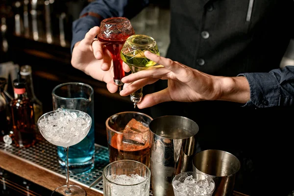 Närbild bartender håller flaskor med sprit och lägger den till glas med cocktail — Stockfoto