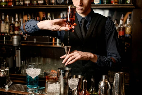 Barkeeper hält Stahlvorrichtung in der Hand und schüttet Getränk aus Flasche hinein. — Stockfoto