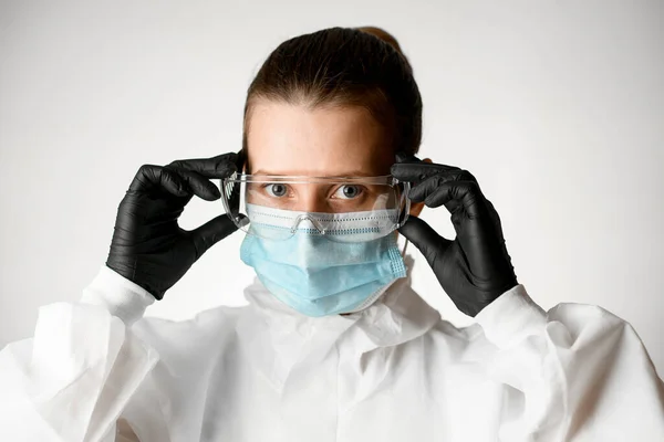 Кормилица в медицинской маске и белый защитный костюм регулирует очки на ее лице — стоковое фото