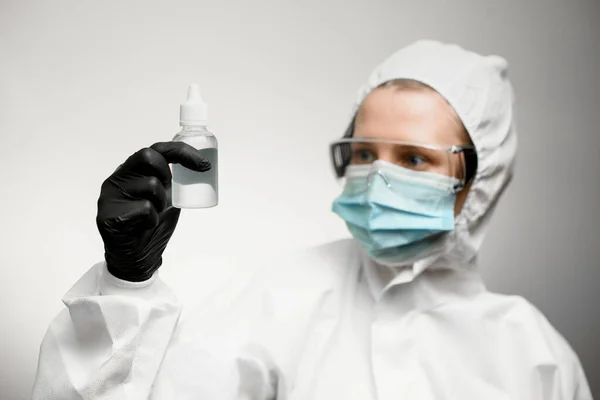 Person in full medical protective clothing holds disinfectant in hand and look at it.