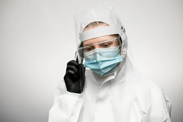 woman in medical protective clothing and black latex glove holds phone near her ear