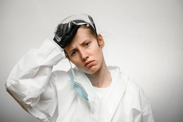 Уставшая женщина медсестра в защитной медицинской одежде с снятой медицинской маской и очками — стоковое фото