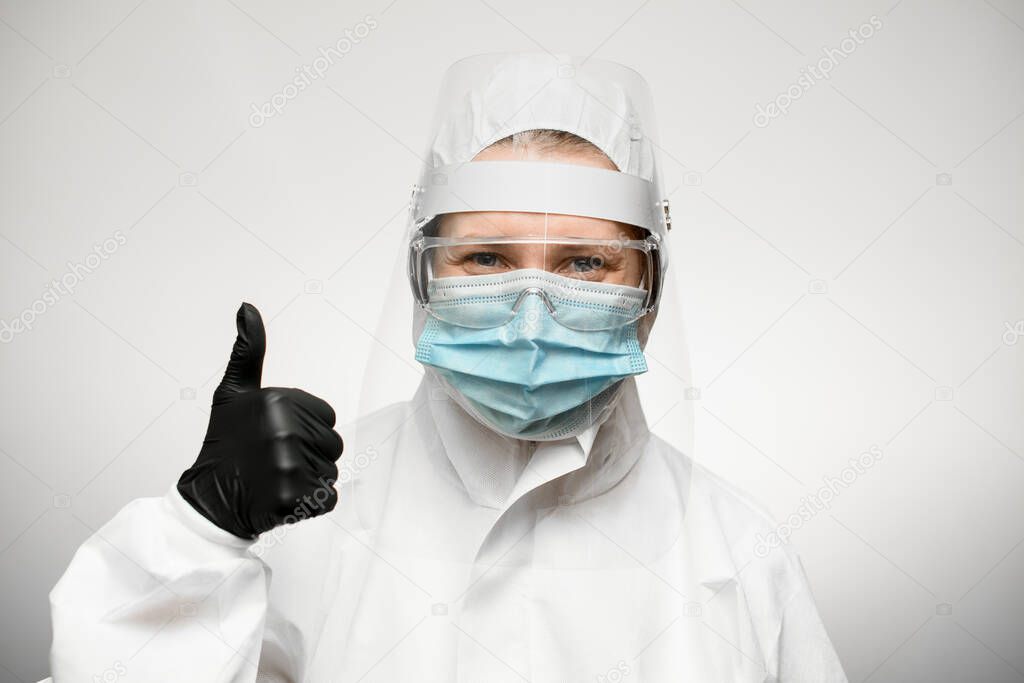 woman in medical protective clothing and black latex glove shows hand thumbs up sign.