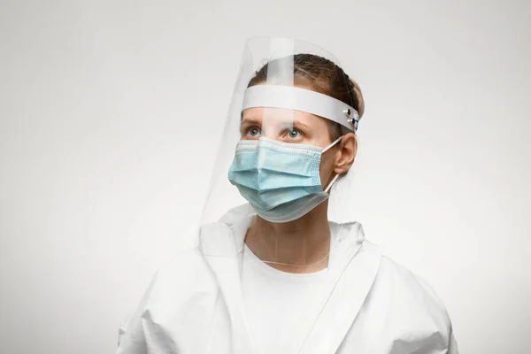 young female nurse in medical mask and protective shield on her head looks away.