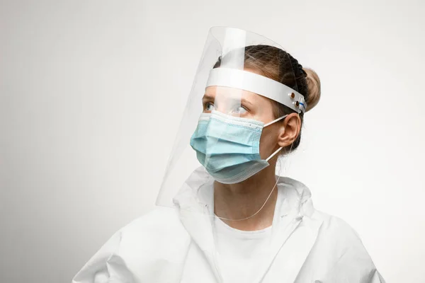 Молодая женщина в медицинской маске и защитный щит на голове смотрит в сторону . — стоковое фото